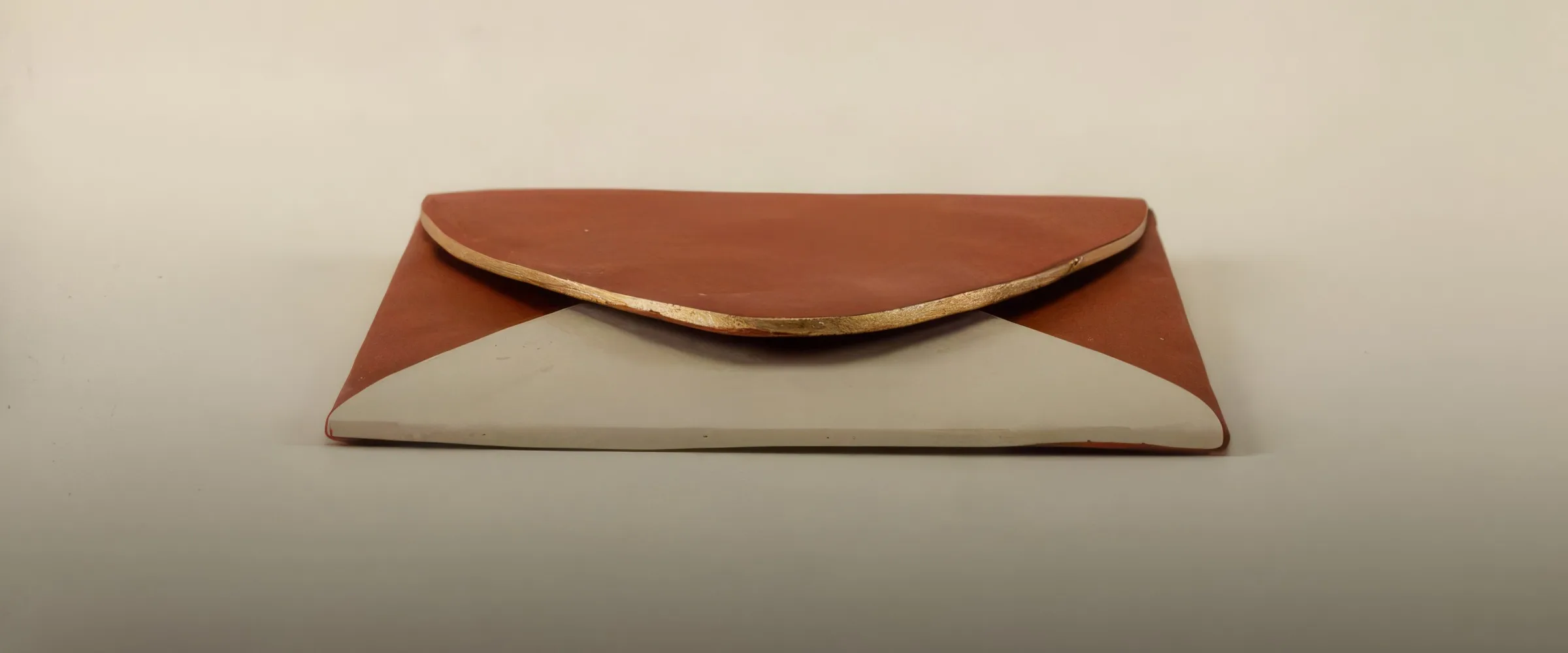 A sealed clay envelope with a gold edge, resting on a table.
